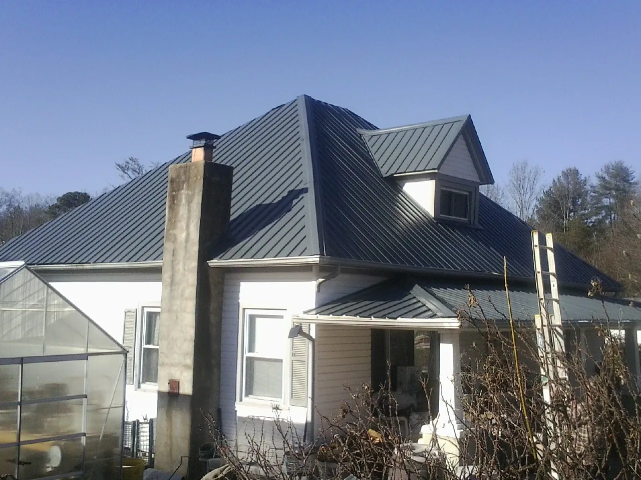 Dark blue standing seam metal roof on a white farmhouse with dormer — Slate & Tile Roof Repair by Roofing Brothers in Flintville