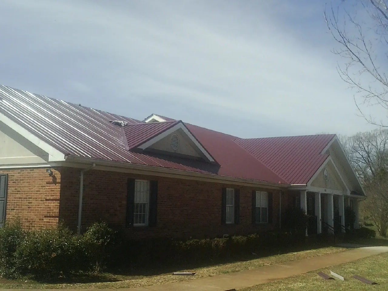 Red metal roof with gabled entries on a long brick building, from a Hail Damage Roof Repair job in Flintville