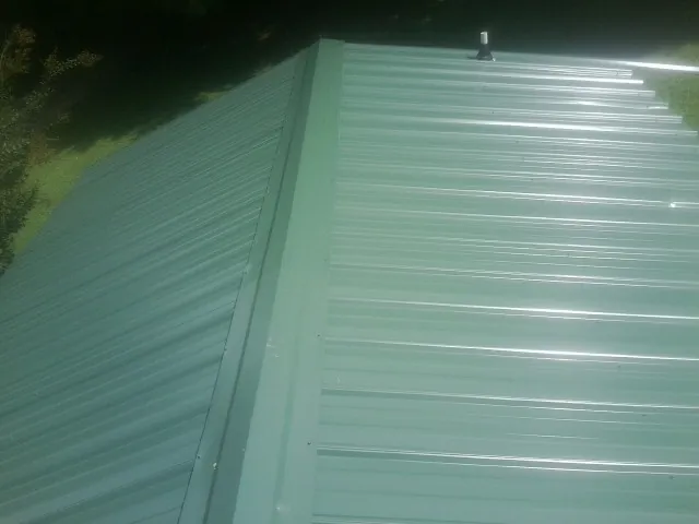 New green metal panels meeting at the ridge of a roof — Flat Roof Repair work by our crew in Flintville