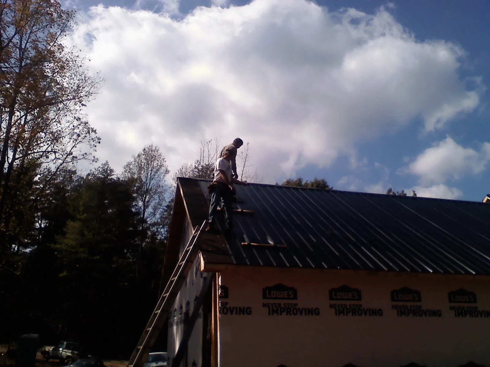 Roofer fastening dark metal panels high against a cloudy sky, from a Roof Inspection job in Flintville