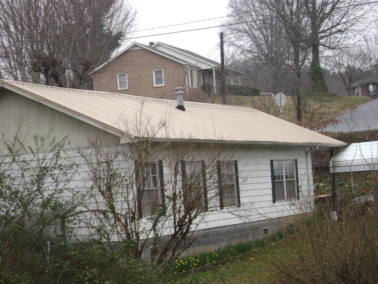 Tan metal roof on a white sided house set into a hillside — Commercial Roofing by Roofing Brothers in Flintville